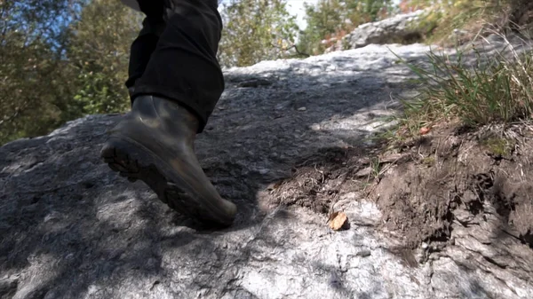 Close up van man rubberen laarzen tijdens het wandelen op pad in de bergen in verdorde gras. Wandelaar mens benen de steile hellingsgraad van de rots klimmen. — Stockfoto