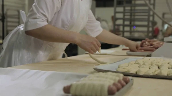 Stäng för en kvinna som inslagning korv i raw smördeg på bageriet. Rå korv rullade degen av kvinna baker händer, förbereda matkoncept. — Stockfoto