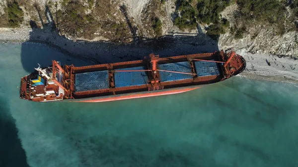 Vista aérea de una barcaza roja y vacía amarrada cerca de la hermosa orilla azul del mar. Gran barco industrial de pie cerca de la colina con árboles verdes . —  Fotos de Stock