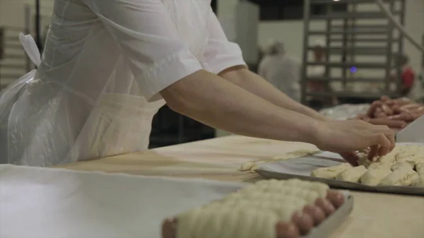 Stäng för korv insvept i raw smördeg på bageriet och baker kvinna rulla ut degen. Rå korv rullade degen av kvinna baker händer, förbereda matkoncept. — Stockfoto