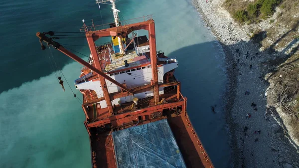 Aerial top view of an empty, red barge moored near the beautiful blue sea shore. Big Industrial ship standing near the hill with green trees. — Stock Photo, Image