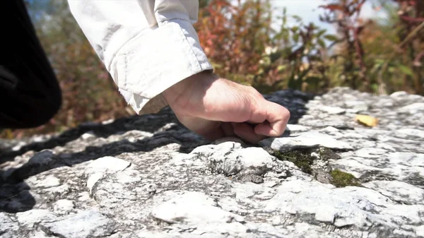 Gros plan pour un randonneur se levant de ses genoux et debout sur un rocher devant de nombreux buissons aux feuilles rouges et vertes. Un homme appuyé sur ses mains pour se lever et se tenir debout sur un rocher . — Photo