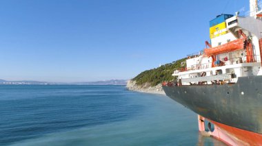 Hava deniz kıyıya yakın yerde bir yamaç boyunca demirlemiş kırmızı, boş barge için mavi gökyüzü arka plan üzerinde yeşil ağaçları ile kaplı. Bir yaz, güneşli günde büyük kargo gemisi için yakın çekim.