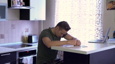 Bar counter mutfakta duygu çok kızgın ve üzgün oturan genç yakışıklı adam. Öfkeli erkek mutfakta oturmuş, düşünme ve atma kağıtları, negatif duygular kavramı.