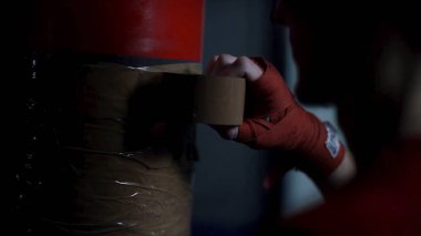 Arkadan Görünüş bir adamın onun boks armut bant karanlık odada, spor kavramı ile sarma tarafından hazırlanıyor. Kum torbası kahverengi yapışkan bant ile kaydırma avcı.