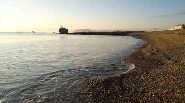 Çakıl ve günbatımı gökyüzü arka plan üzerinde sahilde dalgalar sahil şeridine yakın çekim. Vurdu. Taşlı deniz kıyısında küçük dalgalar ile arka plan üzerinde çok gemi.