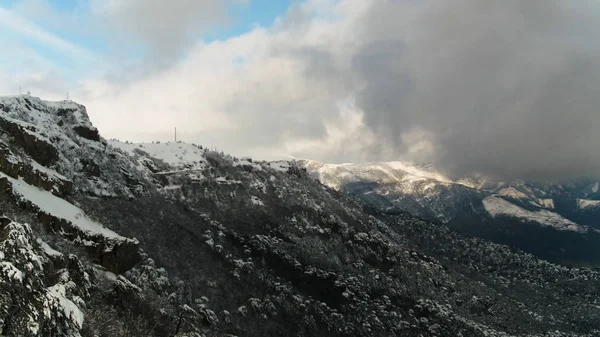 La pente du haut massif rocheux recouvert de pins dans des nuages brumeux. Fusillade. Aérien pour la pente de montagne boisée dans des nuages lourds et gris et fond bleu ciel . — Photo