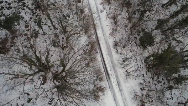 Aereo per la foresta coperta di neve e strada invernale, vista a volo d'uccello. Gli hanno sparato. Vista dall'alto della strada di campagna che attraversa i bellissimi paesaggi innevati . — Foto Stock