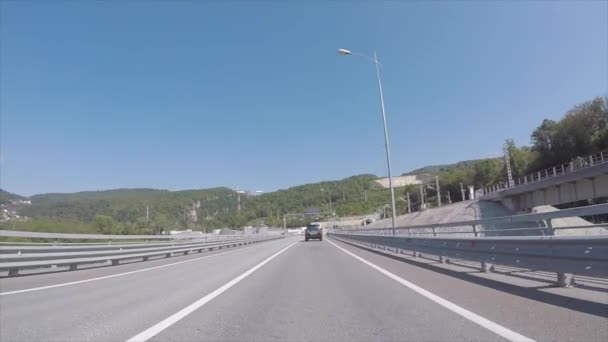 Uitzicht vanaf de auto op een snelweg in de buurt van de trein- en passerende trein tegen blauwe hemel en bergen. Scène. Sotsji, Krasnodar regio, Rusland. — Stockvideo