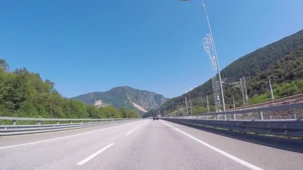 Bilhandel flyttar på en motorväg nära järnvägen mot blå himmel och Kaukasiska bergen. Scen. Sochi, Krasnodar region, Ryssland. — Stockvideo