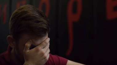 Yüzünü bir palm kırmızı sembolleri ile siyah duvara ile kapsayan stresli bir genç adam portresi. Adam facepalm yapma jest karanlık duvar arka plan üzerinde.