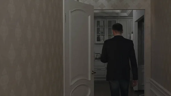 Rear view of a young man in his apartment going through corridor to the kitchen. Male in suit going to the kitchen in small flat.