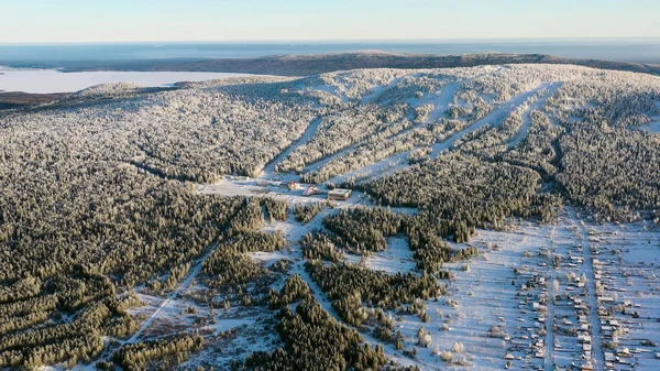 Aérea de la estación de esquí con funicular en el bosque nevado en un día soleado. Filmación. Paisaje invernal de montaña nevada entre pinos sobre fondo azul del cielo . — Foto de Stock