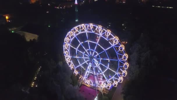 Amusement Park légi lövés éjszakai város fényei. Klip. Légifelvételek gyönyörű óriáskerék elejére helyezi a háttér világítás fel a nyári este — Stock videók