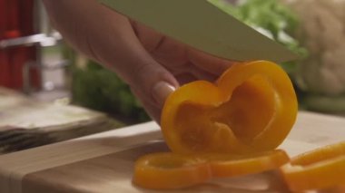 Baş kesme sarı bir ahşap tahta üzerinde profesyonel bir bıçak ve büyük bir beceri ile biber. Sahne. Şef salata sağlıklı yemek yapma ve dolmalık biber kesme tahtası üzerinde doğrama yakın çekim