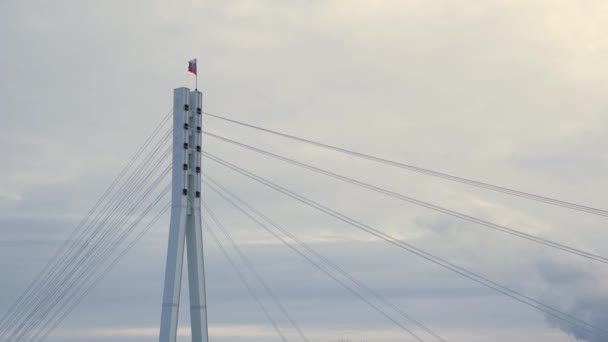 Bandera de la Federación Rusa ondeando en el viento en la parte superior del puente. Acciones. Bandera rusa en la parte superior de un puente sobre fondo gris, cielo nublado . — Vídeos de Stock