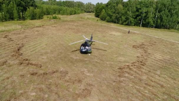 L'elicottero si aggira sul campo. L'elicottero atterrò sul campo vicino alla cintura forestale. Elicottero atterrato su erba gialla, giorno nuvoloso — Video Stock