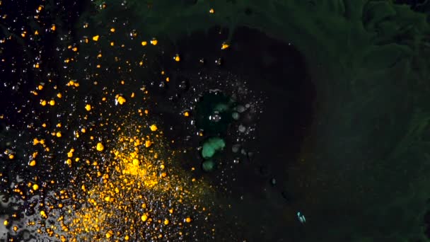 Drops of liquid soap falling in black substance with yellow dry inks floating on the surface. Colorful reaction on mixing inks and soap. — Stock Video