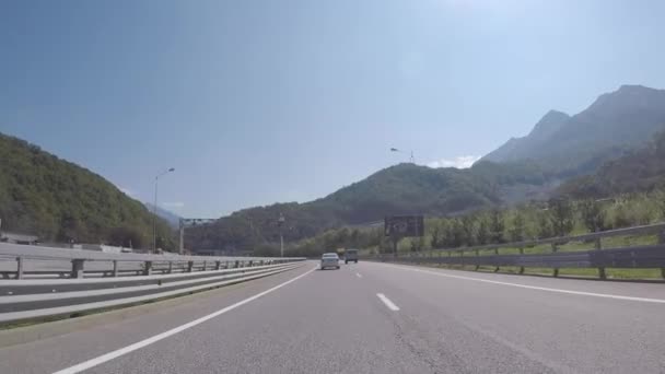 Vue sur une route menant au village olympique de montagne à partir d'une voiture en mouvement avec des montagnes hautes et anciennes sur le fond contre le ciel bleu. Scène. Belle journée ensoleillée . — Video