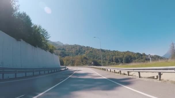 Vue de la voiture tournant à gauche sur une autoroute sous le téléphérique sur le fond des belles montagnes couvertes d'arbres et d'arbustes. Scène. Merveilleux voyage d'été . — Video