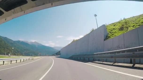 Bekijk op een weg vanuit de auto langs een high-speed snelweg met witte stenen barrière haasten van de ene kant tegen blauwe heldere hemel in de zomer. Scène. Reizen met de auto. — Stockvideo
