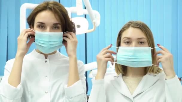 Zahnärztinnen, die sich eine Maske aufsetzen und direkt in die Kamera schauen. schöne junge Ärztinnen in Uniform, die im Zahnkabinett stehen, Medizin und zahnärztliches Versorgungskonzept. — Stockvideo