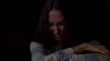 Dizlerinin sarılma ve koyu arka plan üzerinde yalnızlık kavramı ağlayan üzgün, genç bir kadın portresi. Depresif kadın tek başına oturmak ve karanlık duvara ağlama.