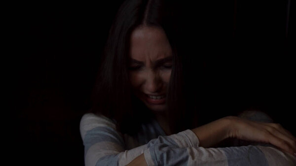 Портрет грустной молодой женщины, обнимающей колени и плачущей на тёмном фоне, концепция одиночества. Депрессивная женщина сидит одна и плачет о темной стене
.