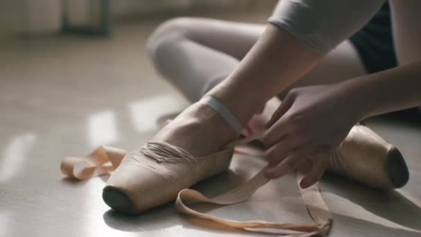 Close-up of ballerinas feet on a light wooden floor. Girl tying ribbon of pointe shoes. — Stock Video