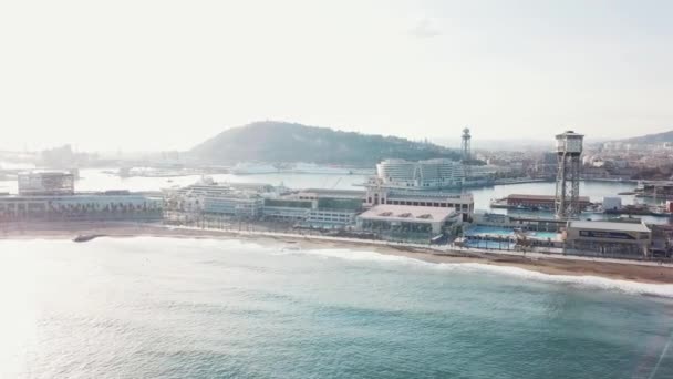 美しい沿岸都市、近代的な建物、ターコイズ ブルーの海の波、背景に青い空と山とビーチの上を歩く人々 のビュー。在庫があります。リゾート シーズン. — ストック動画