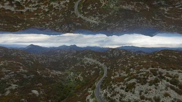 Vista aérea de muitas montanhas altas e da estrada, efeito horizonte espelho. Bela paisagem com rochas e a estrada no céu nublado backgroun, tema de criação . — Fotografia de Stock