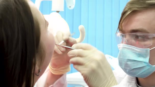 Detailní záběr zubů vyšetření v ordinaci se speciálním vybavením. Muž zubař zkoumání zuby mladé ženy sedící v křesle, koncept zubní péče.