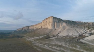 Güzel bir akşam yüksek gri dağ kayalıklarla ve mavi gökyüzü karşı kırsal road yakınındaki yeşil ova görünümünü. Vurdu. Alttan görüntülemek.