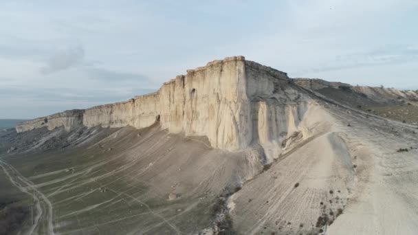 Vista dal basso su un'alta montagna grigia vicino a una pianura verde e strade contro il cielo blu. Gli hanno sparato. Campagna paesaggio montano . — Video Stock