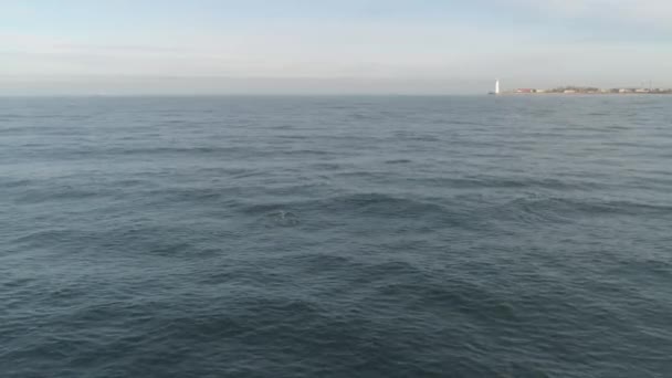 Arka planda bir kıyı şeridi ile gün batımından önce su yüzeyinin görünümü. Atış. Güzel deniz manzarası. — Stok video