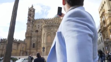Mavi ceket alarak resmi tatil, turizm kavramı sırasında katedral smartphone ile genç adam. Hisse senedi. Bir adam bir fotoğraf kilise telefonda güneşli bir günde yapar.