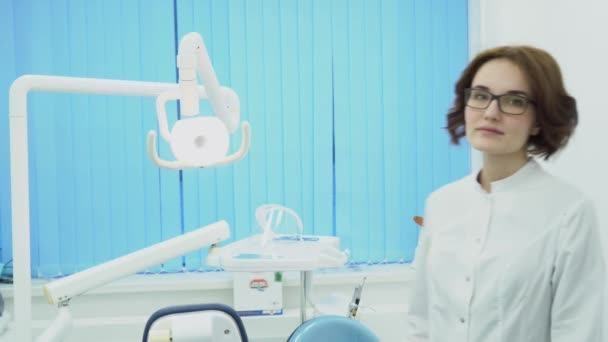 Γυναίκα οδοντίατρος συναντά πελάτη χαμογελώντας. Μέσα μαζικής ενημέρωσης. Γυναίκα οδοντίατρος στο λευκό παλτό καλωσορίζει στο οδοντιατρείο: το νέο πρόγραμμα-πελάτη. Οδοντιατρική έννοια — Αρχείο Βίντεο