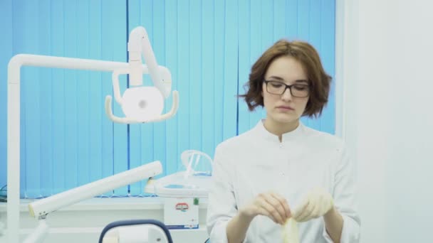 La dentista se pone guantes en el consultorio dental. Medios. Mujer dentista en uniforme se pone guantes de lavado antes de empezar a trabajar — Vídeo de stock