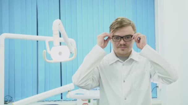 Le dentiste porte des lunettes sur le fond de l'équipement dentaire. Les médias. Jeune dentiste met des lunettes et salue avec sourire dans le cabinet dentaire — Video