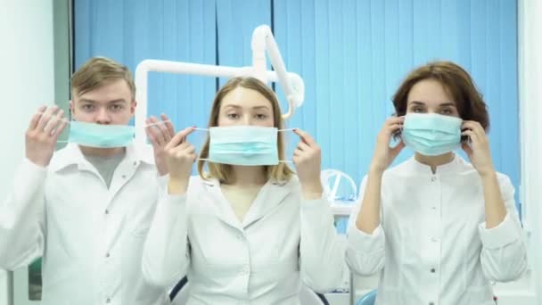 Equipe de médicos com braços cruzados de pé com máscaras. Mídia. Três médicos ficam em poses confiantes com máscaras no fundo do quarto do hospital — Vídeo de Stock