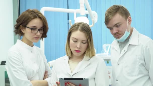 El equipo de médicos discute diagnósticos de pacientes. Medios. Los médicos analizan conjuntamente las pruebas y los diagnósticos de los pacientes en el fondo de la habitación de hospital con lámpara — Vídeo de stock