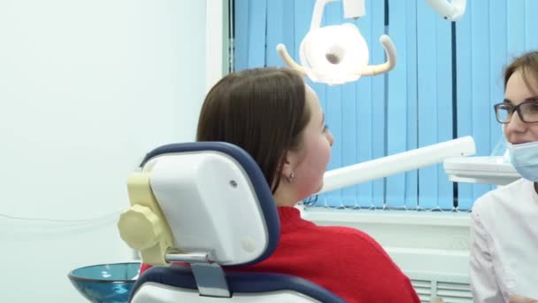 Mujer dentista hablando con paciente. Medios. Mujer dentista consulta a paciente sobre tratamiento antes de comenzar el trabajo — Vídeos de Stock