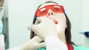 Kadın ile çalışan diş hekimi close-up. Medya. Diş hekimi diş hijyeni genç kadın yapar. Diş hekimi hastanın ağzına onun şırınga yapışır. Ağız ve diş tedavi ve bakım