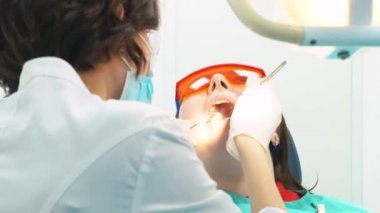 Genç kadın dişçi diş ofisinde bir diş için Bayan genç hasta temizlik yapma close-up. Diş Bakımı.