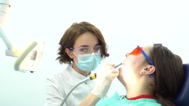 Mujer dentista pule los dientes de la paciente. Medios. Atractivo dentista pule sus dientes con cepillo antes del procedimiento de blanqueo con equipo profesional — Vídeos de Stock