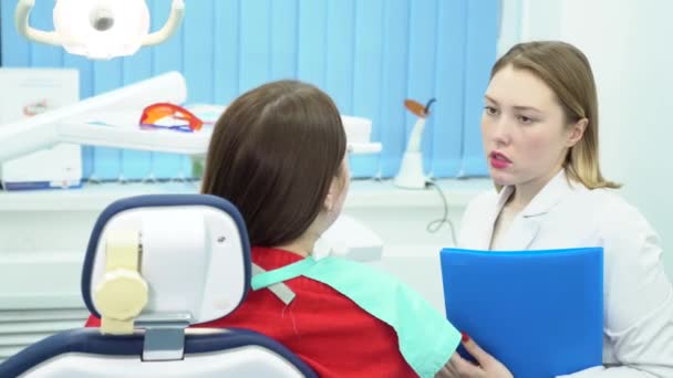 O dentista discute o tratamento com o paciente. Mídia. Dentista segurando pasta com testes de pacientes aconselha e prescreve tratamento — Vídeo de Stock