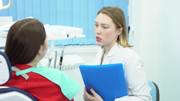 O dentista discute o tratamento com o paciente. Mídia. Dentista segurando pasta com testes de pacientes aconselha e prescreve tratamento — Vídeo de Stock