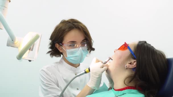 Primer plano de la joven dentista en el consultorio dental haciendo una limpieza de dientes a la joven paciente femenina. Cuidado dental . — Vídeos de Stock