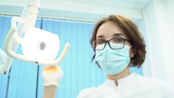Vista inferior del dentista femenino. Medios. Atractiva mujer dentista encender lámpara electrónica examina pacientes cavidad oral — Vídeo de stock