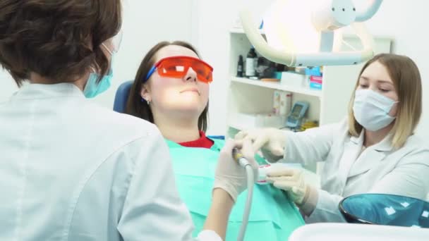 Close-up da equipe de dentista médica em consultório odontológico fazendo uma limpeza dos dentes para o paciente jovem do sexo feminino. Cuidados dentários . — Vídeo de Stock